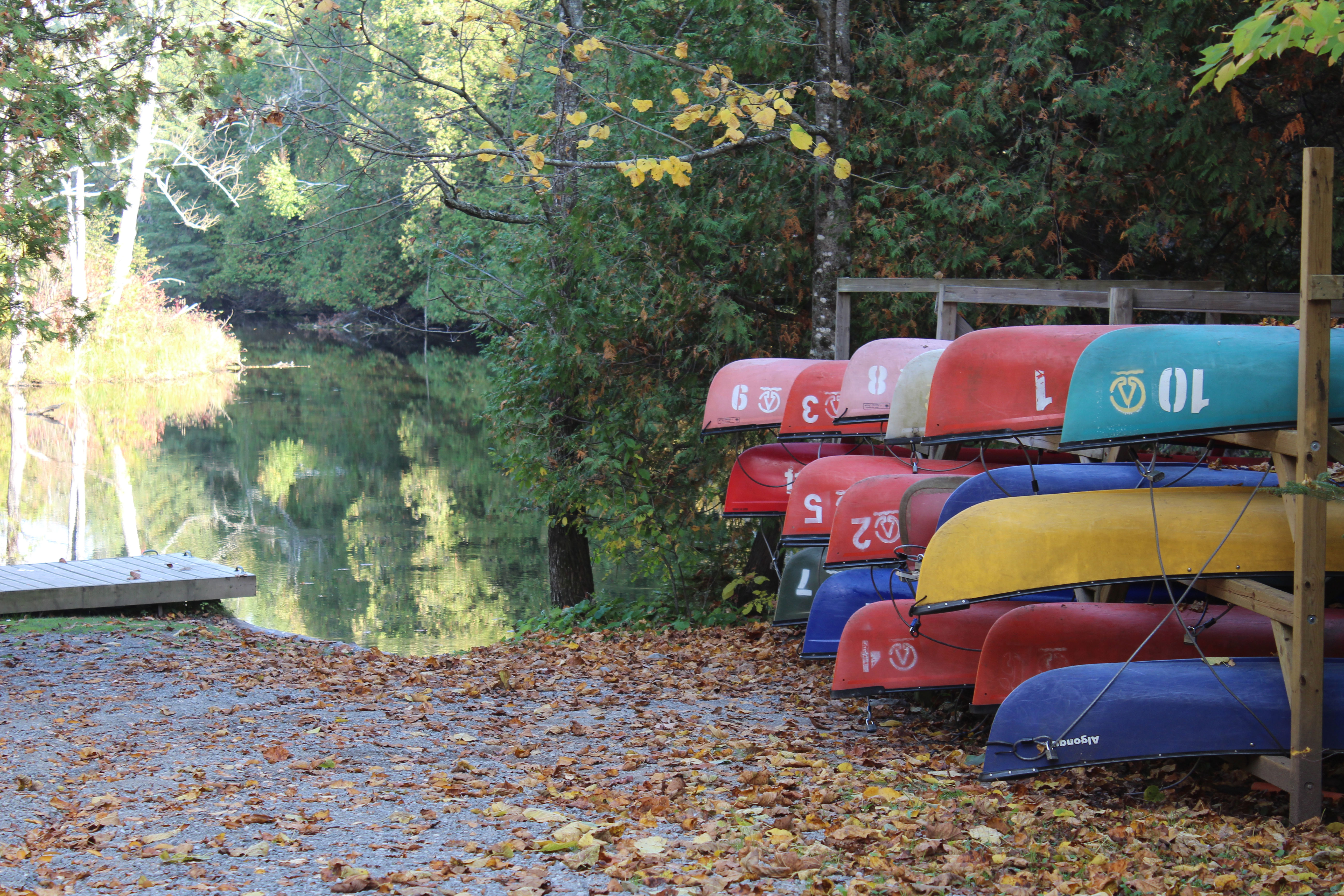 Colourful canoes and kayaks on a stand beside a dock and boat launch along the Indian River at Warsaw Caves Conservation Area.